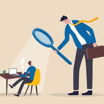 Illustration of large besuited figure holding a magnifying glass looming over a much smaller besuited figure working at a desk, representing Ofsted inspections