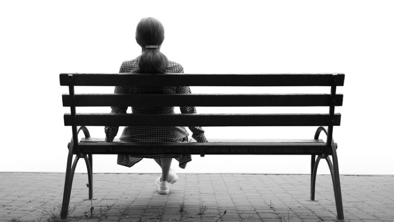 Photo of lonely figure sat on park bench, representing school absence
