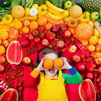 Kid surrounded by rainbow of fruit for Healthy Eating Week